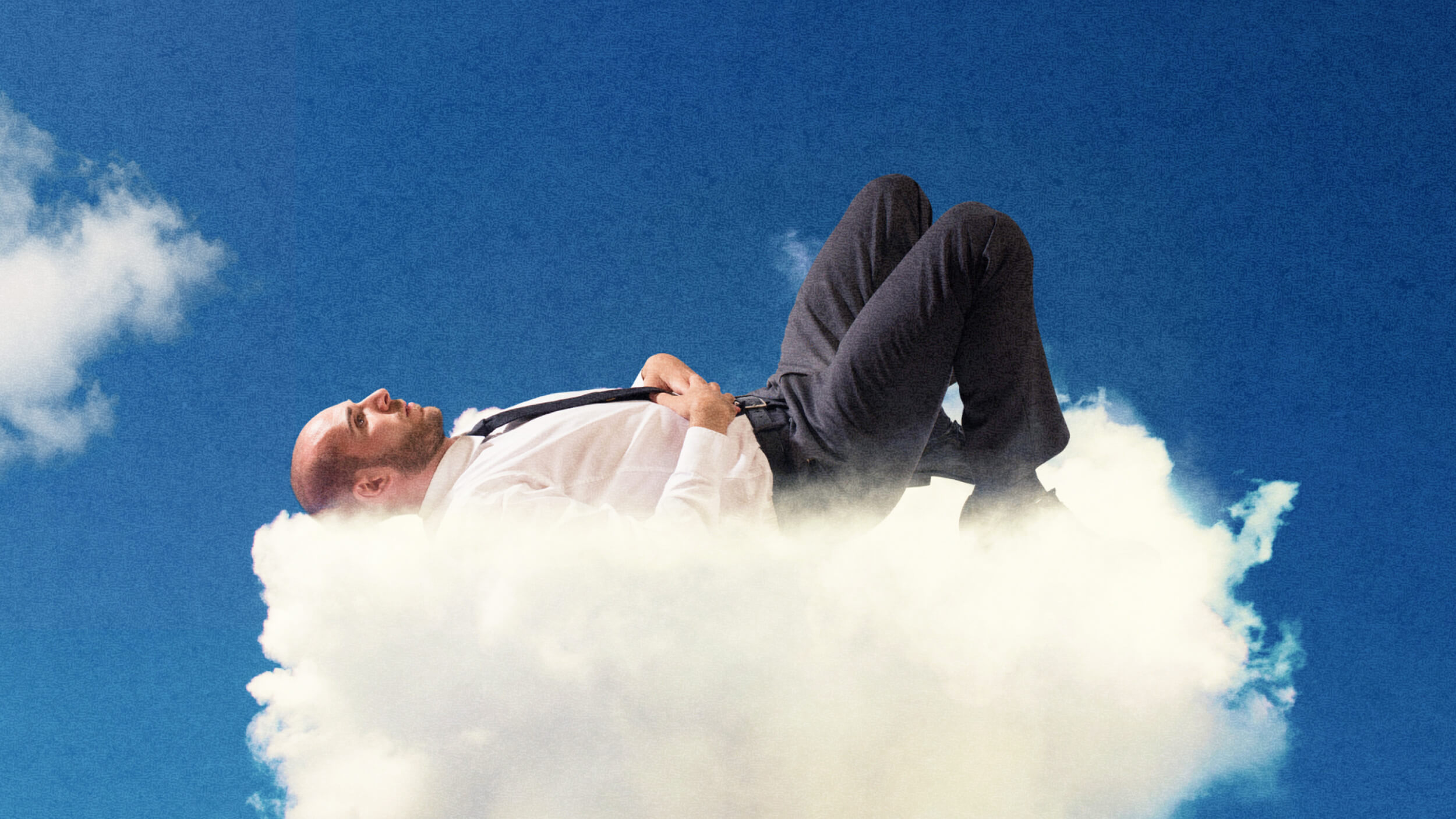 A man in business attire lies relaxed on a cloud against a clear blue sky, embodying inner stillness.