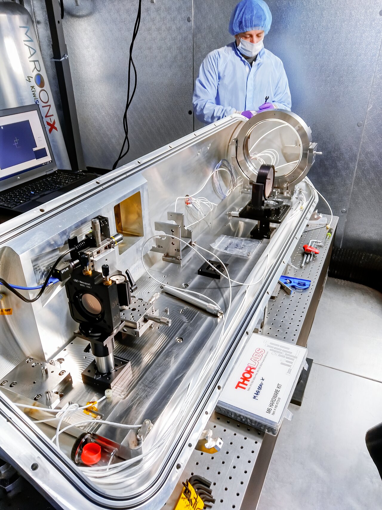 A person in protective gear works in a lab with scientific equipment on a stainless steel table, conducting research that could help us learn more about exoplanets orbiting the nearest single star.