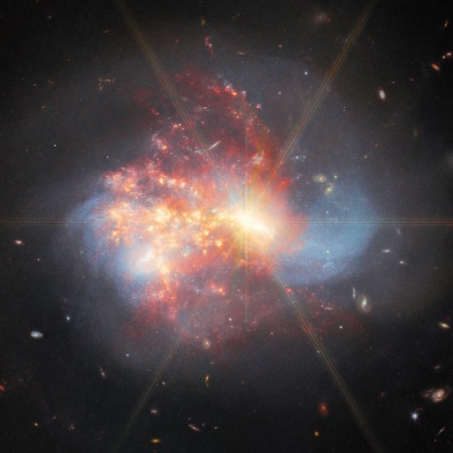 A vivid image of a bright, colorful galaxy with swirling red, blue, and white clouds of gas and dust, where galaxies collide amid distant stars in the dark, expanding universe.