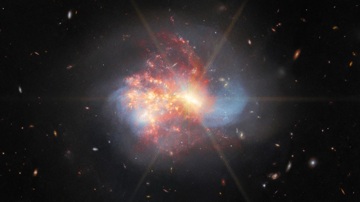 A vivid image of a bright, colorful galaxy with swirling red, blue, and white clouds of gas and dust, where galaxies collide amid distant stars in the dark, expanding universe.