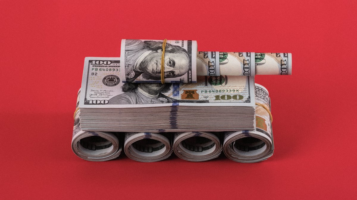 A miniature tank made from rolled and stacked U.S. hundred-dollar bills is displayed on a red background.