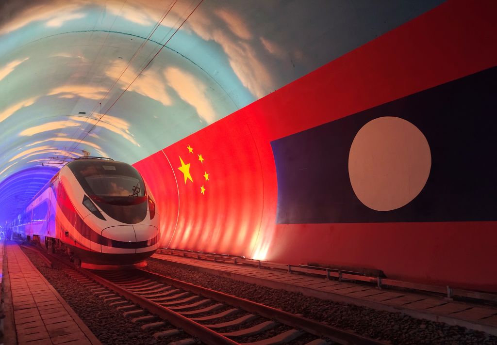 A modern train travels through a tunnel decorated with the national flags of China and Laos illuminated on the walls.