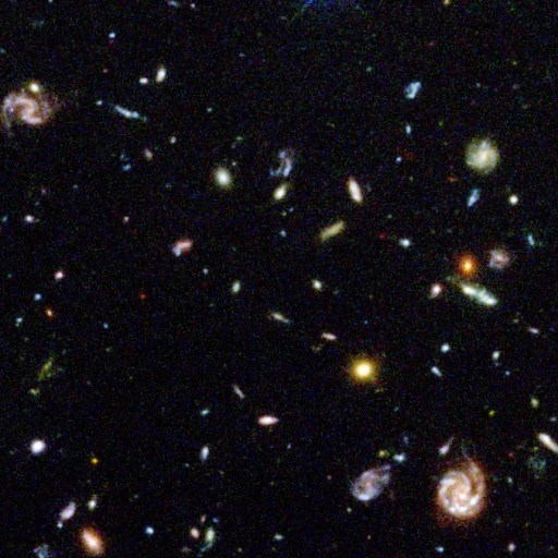 A vast view of deep space, captured in one of NASA's most important images, displays numerous galaxies of varying shapes and colors against a dark backdrop scattered with distant stars.