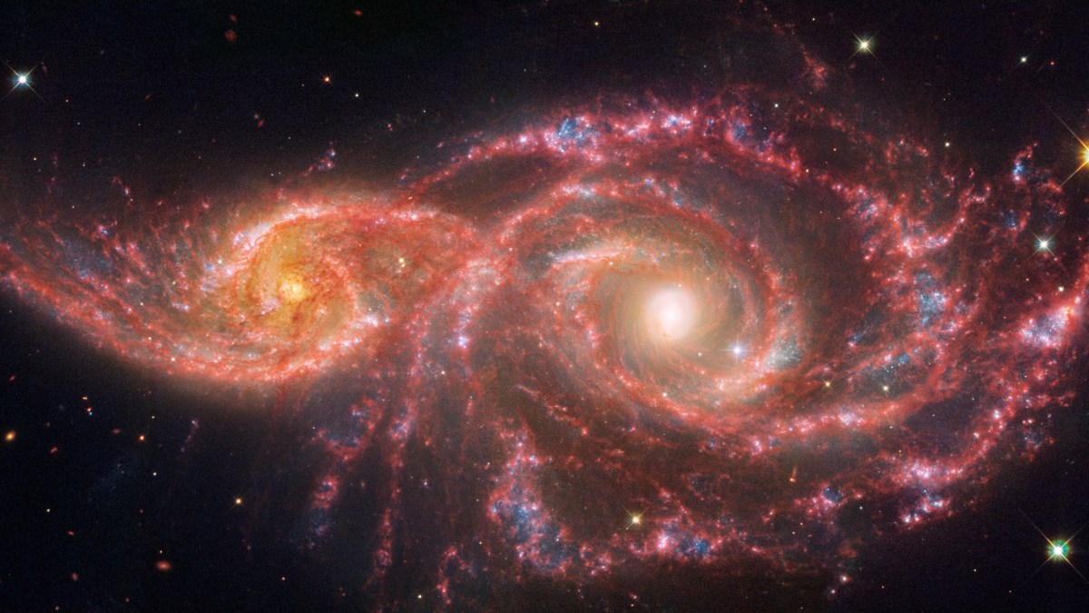 Two colorful spiral galaxies interacting in space, with bright centers and swirling arms of red, blue, and white hues, set against a backdrop of stars.