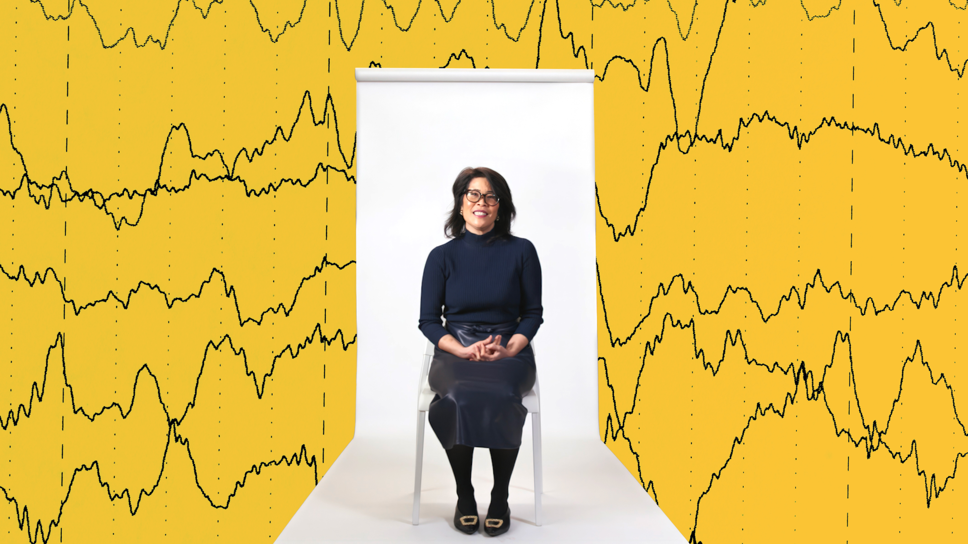 A woman sits on a chair against a white backdrop, with yellow graphics of brain wave patterns in the background.