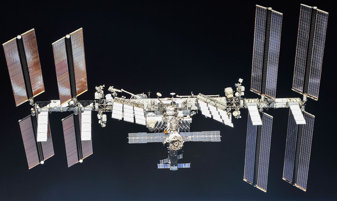 The International Space Station orbits Earth, displaying its large solar panels and modular structure against a black background.