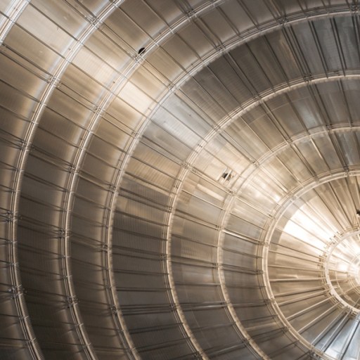 Close-up of a large, metallic, circular structure with concentric rings and radial lines, illuminated by natural light from one side—evoking experiments that revealed the neutrino mass is smaller than once believed.
