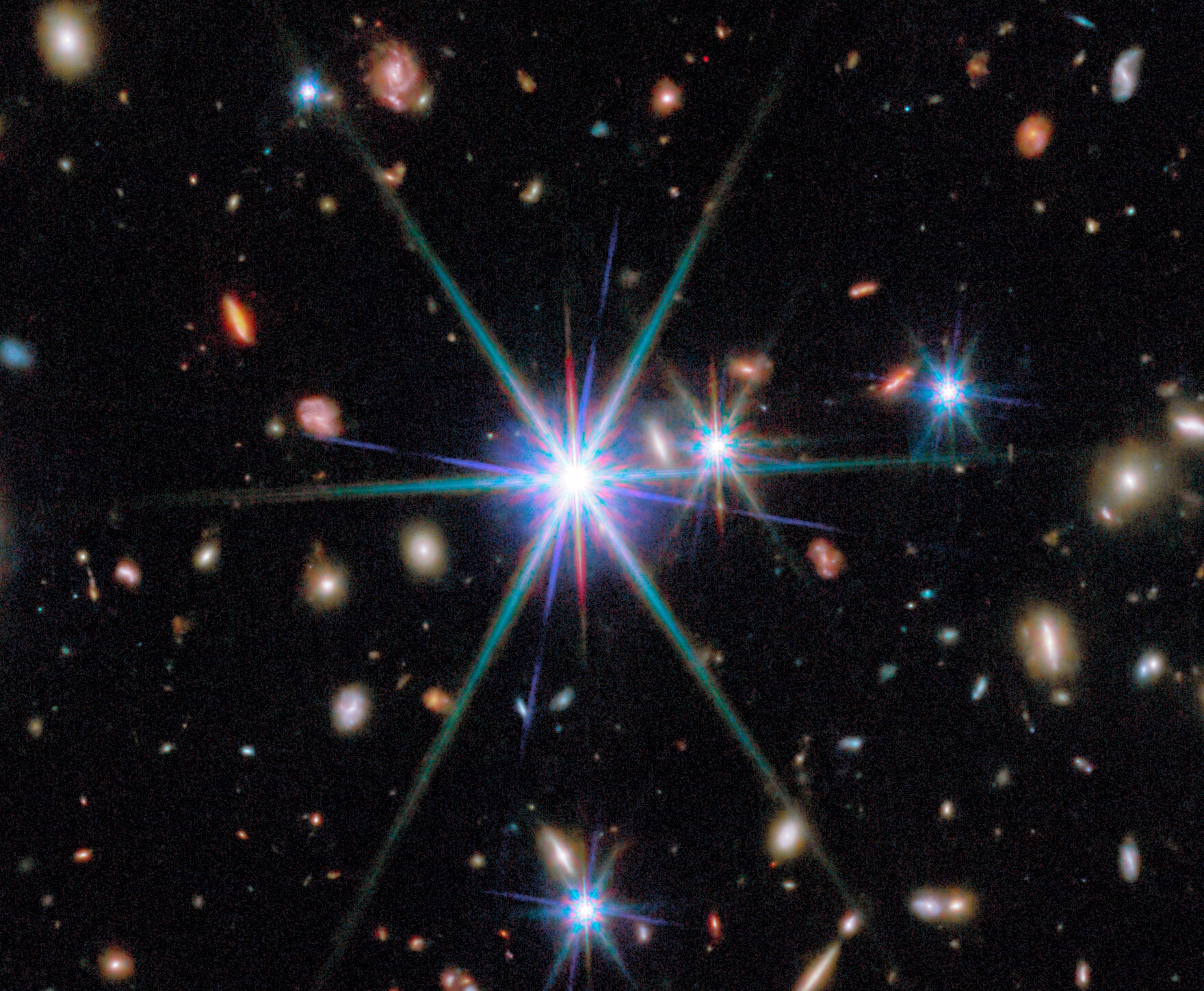Bright stars with diffraction spikes are surrounded by numerous distant galaxies scattered across a dark background in deep space.