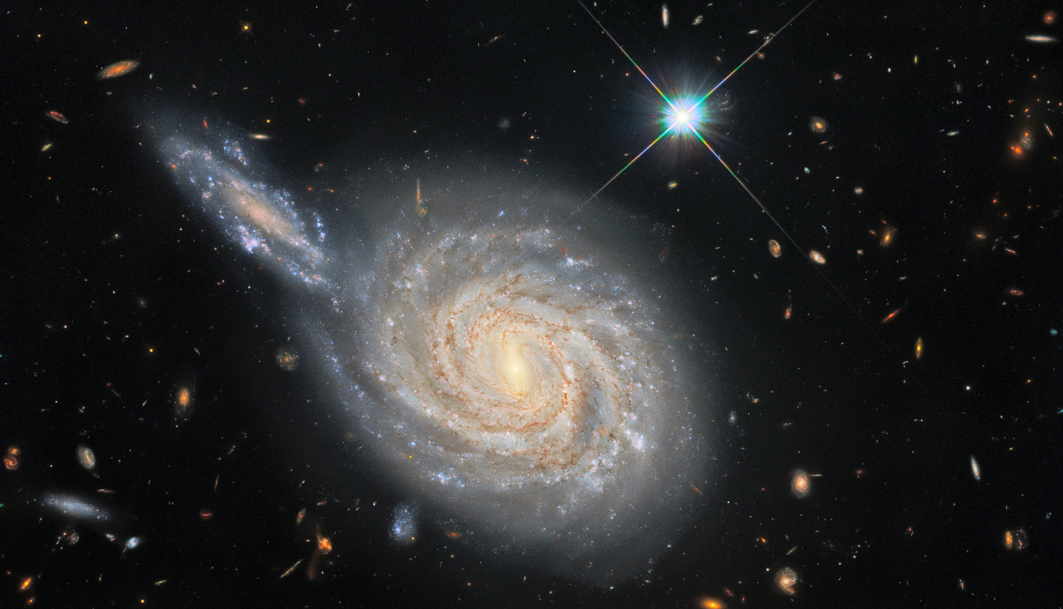 Spiral galaxy with a bright core and extended arms, its space appearance enhanced by numerous stars and distant galaxies against a black background that could easily deceive the eye.