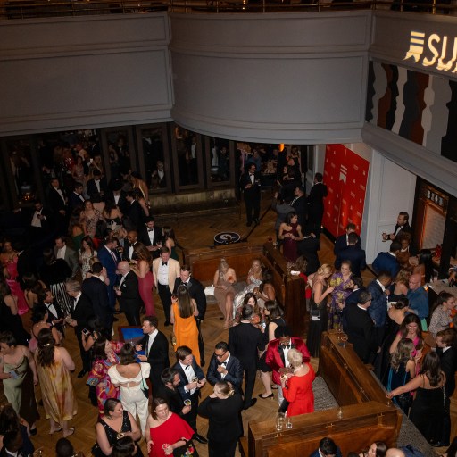 Large crowd of well-dressed people socializing at an indoor event; "Substack" is projected on a wall above.