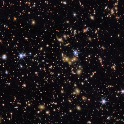 A dense field of stars and galaxies is visible against a black background, with some bright stars showing lens flares.