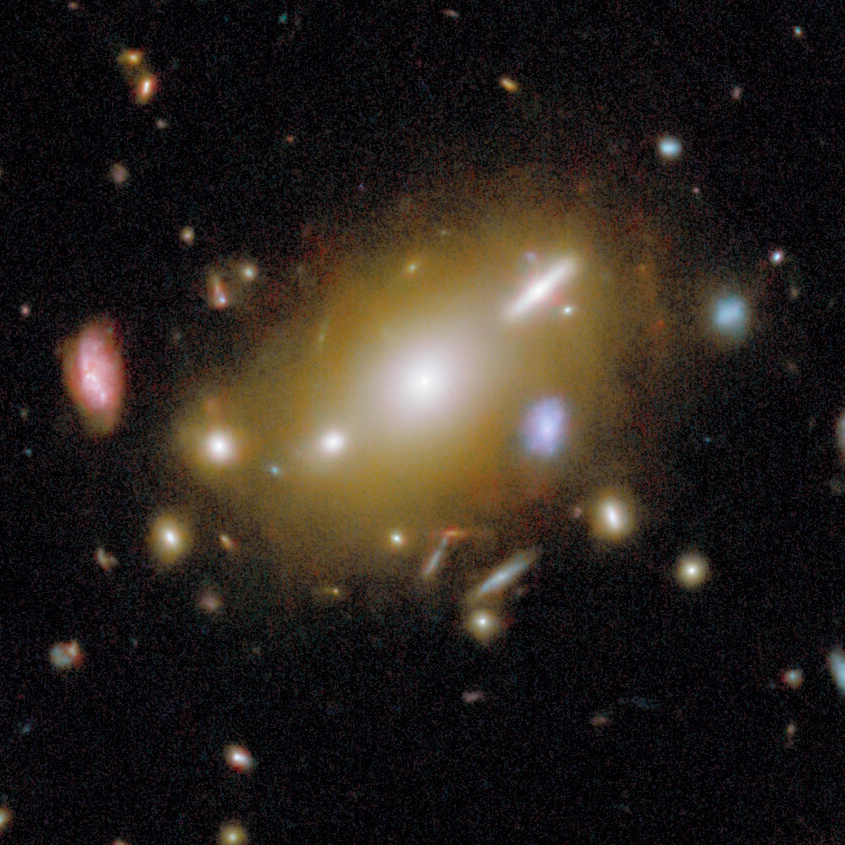 A large, bright elliptical galaxy is surrounded by several smaller galaxies and star clusters against a dark space background.