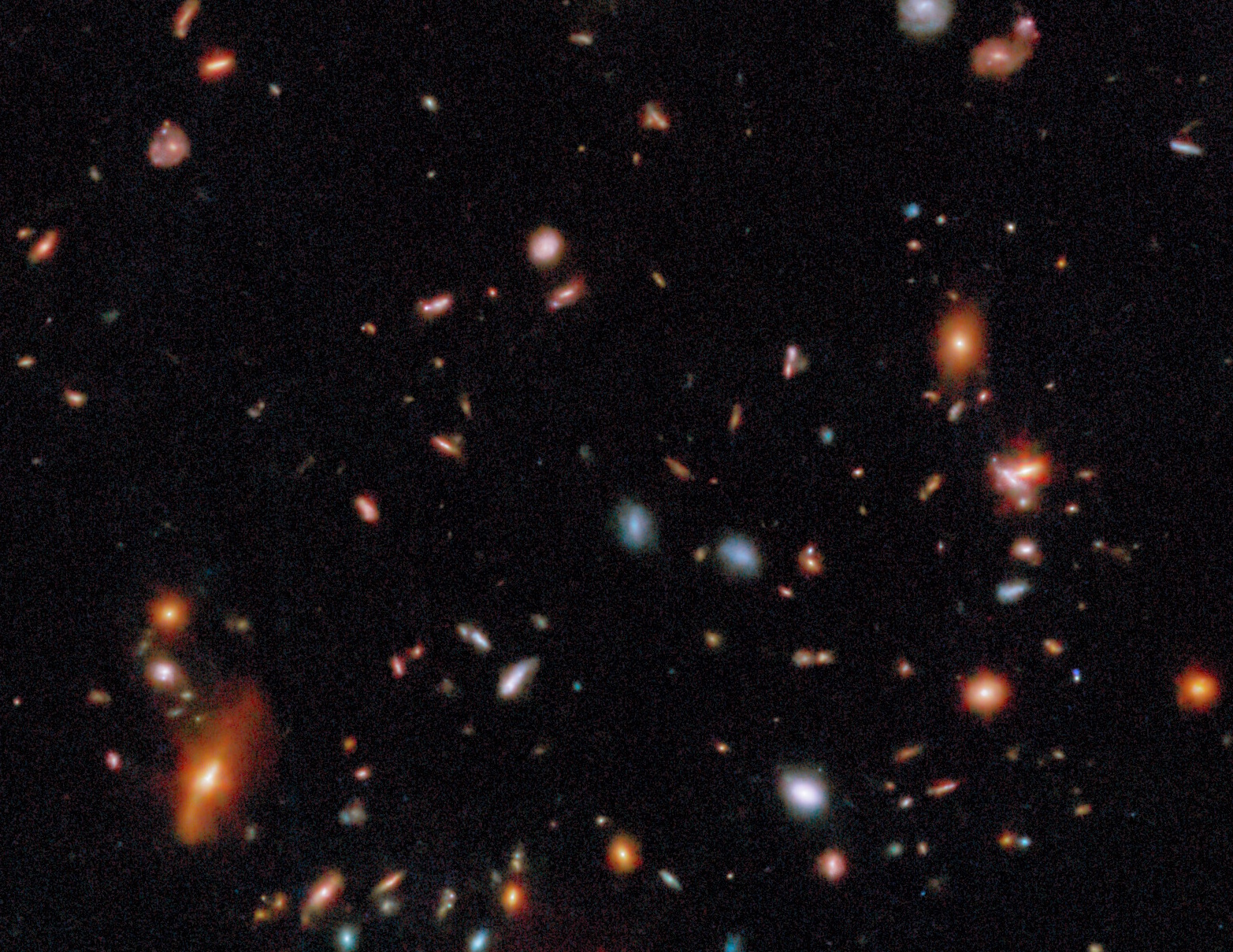 Numerous galaxies and stars of varying colors and brightness are scattered across a dark background in deep space.