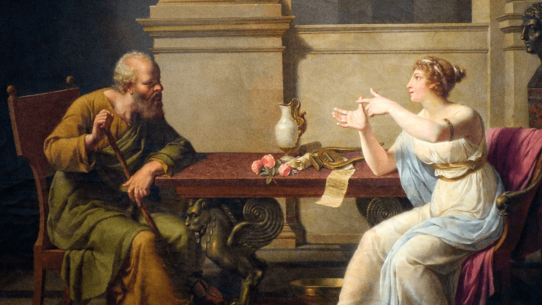 A man and a woman in ancient attire sit at a table indoors, engaged in conversation; beside the jug, roses, and scroll lies a small straw man figure.
