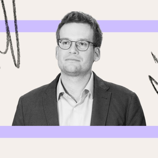 A man in glasses and a suit jacket, resembling John Green, stands in front of a light background with a purple rectangle and abstract black lines.