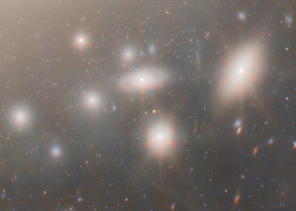A field of bright elliptical galaxies, captured by JWST, appears against a star-filled background in space, with glowing halos surrounding several galaxies due to the most extreme gravitational lens effects.