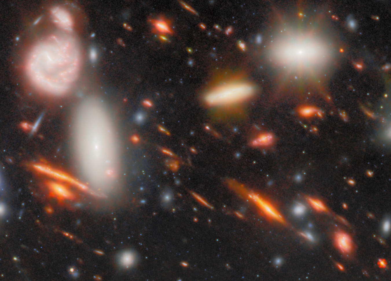 A deep space image from JWST shows numerous galaxies of varying shapes and colors, with bright, glowing stars and hazy, elongated light patterns&mdash;evidence of the most extreme gravitational lens&mdash;against a dark background speckled with small stars.