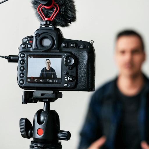 A person is being recorded on video by a camera mounted on a tripod, with the display highlighting visual literacy as the subject appears in focus and the background is artfully blurred.