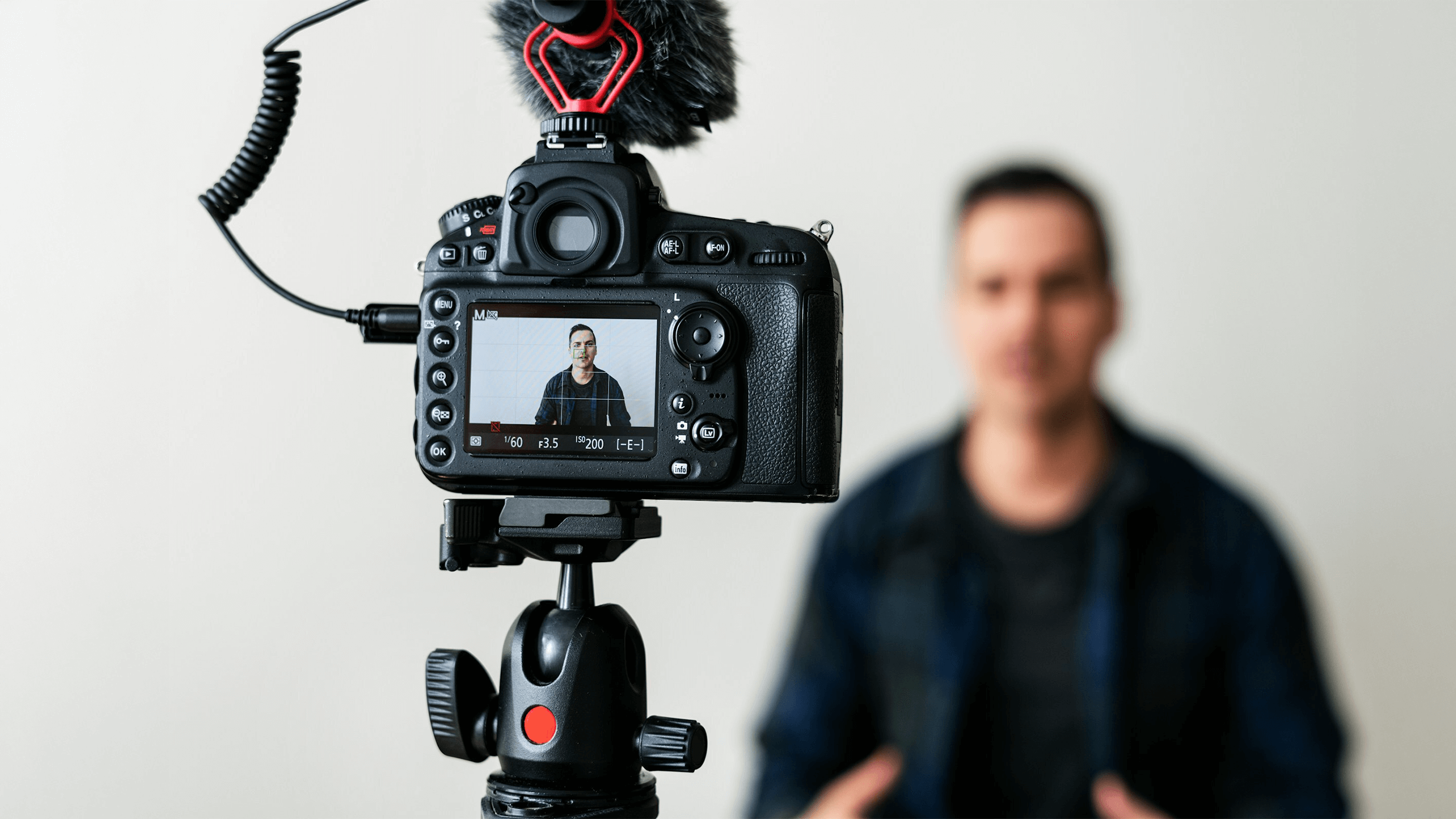 A person is being recorded on video by a camera mounted on a tripod, with the display highlighting visual literacy as the subject appears in focus and the background is artfully blurred.