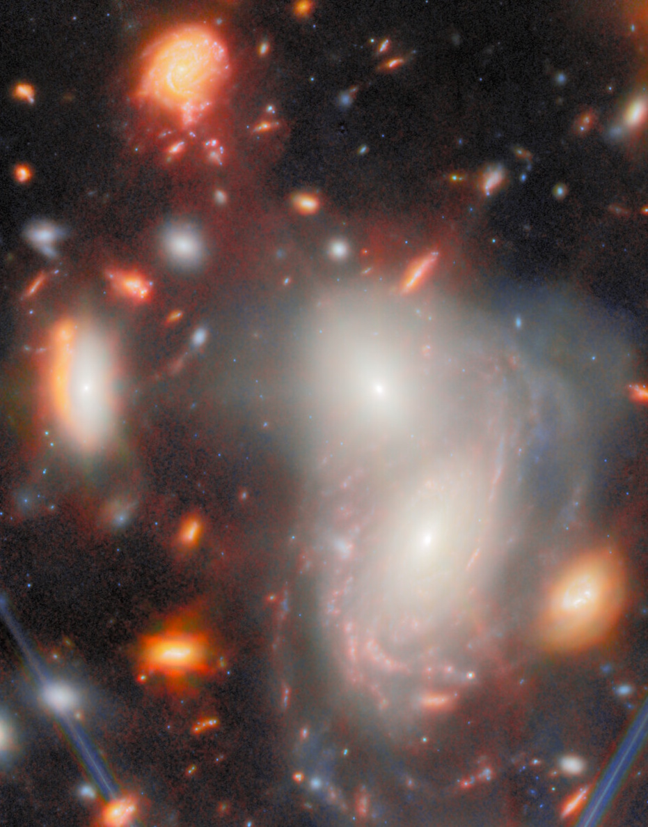 A cluster of bright and colorful galaxies with spiral structures and glowing regions, revealed by the JWST&rsquo;s most extreme gravitational lens, set against a dark space background dotted with stars.