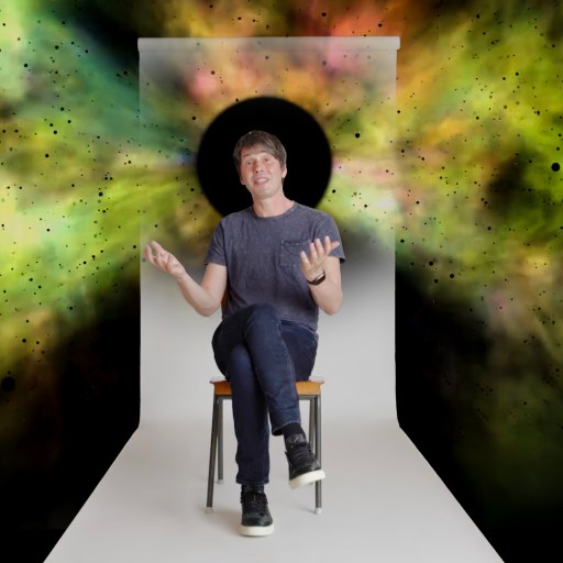 A man sits on a stool in front of a white backdrop with a black circle behind his head, surrounded by colorful, nebula-like clouds.