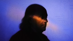 A silhouette profile of a person with long hair against a blue background featuring faint circuit board patterns; a warm light highlights their face.