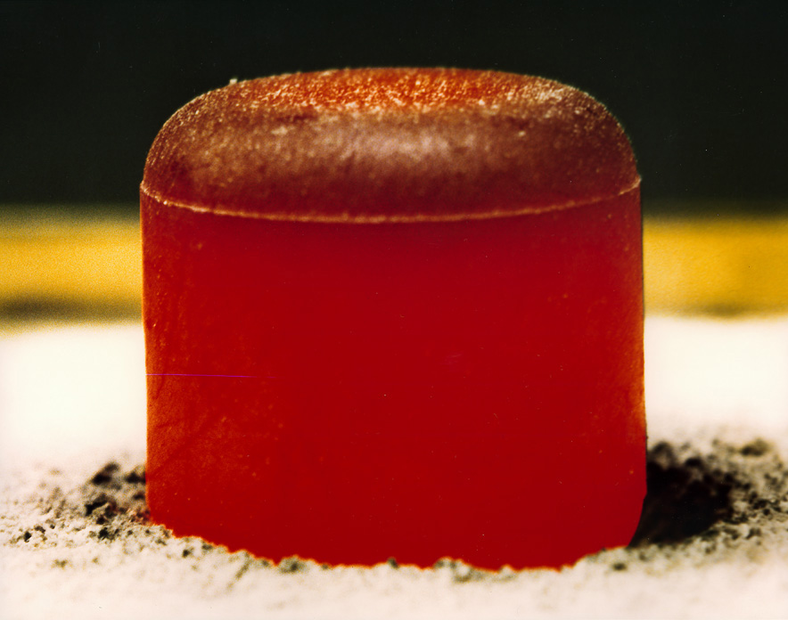 A close-up of a cylindrical, reddish-brown solid object with a rounded top, resting on a surface dusted with dark powder&mdash;resembling something you might find during a mission to Uranus or Neptune.