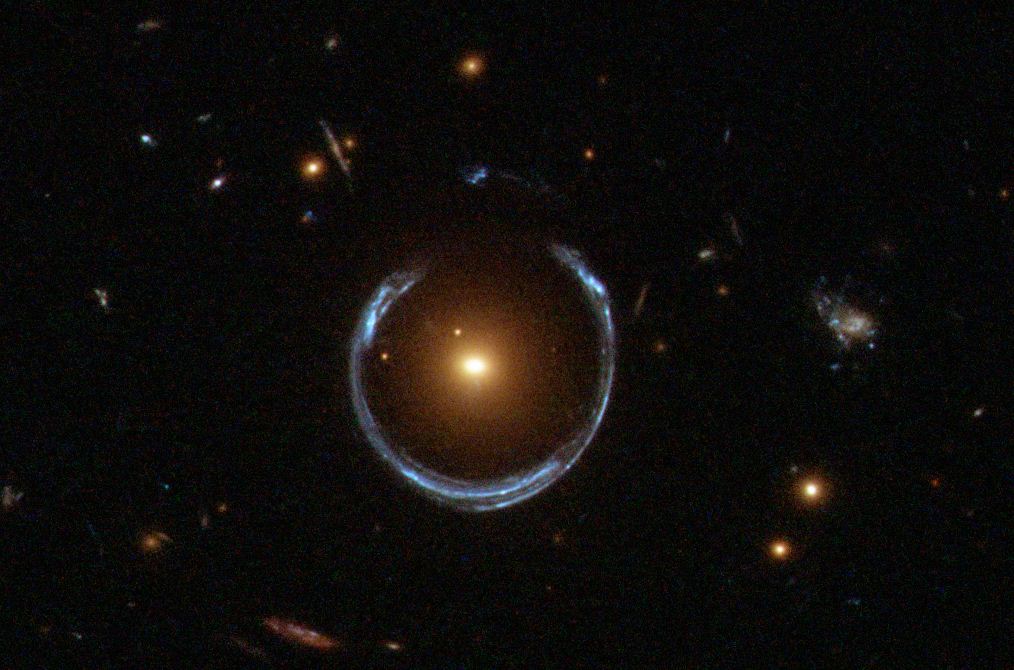 A bright galaxy at the center, possibly hiding the heaviest black hole, bends light from another galaxy behind it to form an Einstein ring&mdash;a striking blue circle surrounded by stars and galaxies.