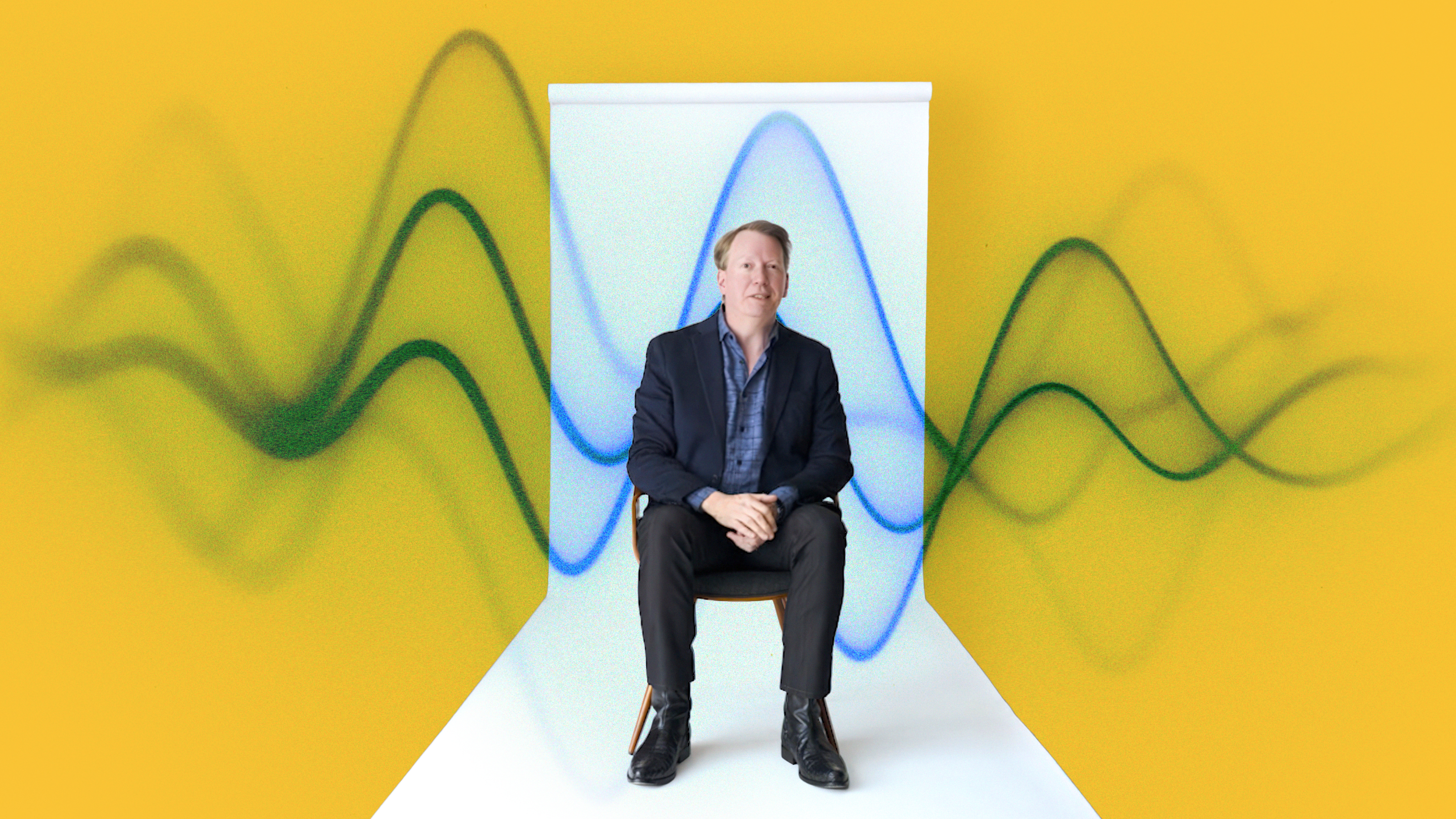A man in a suit sits on a chair against a yellow background with abstract blue and green wave patterns behind him.