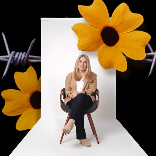 A woman sits on a chair in a studio with a neutral backdrop, overlaid with yellow flowers and barbed wire against a black background.