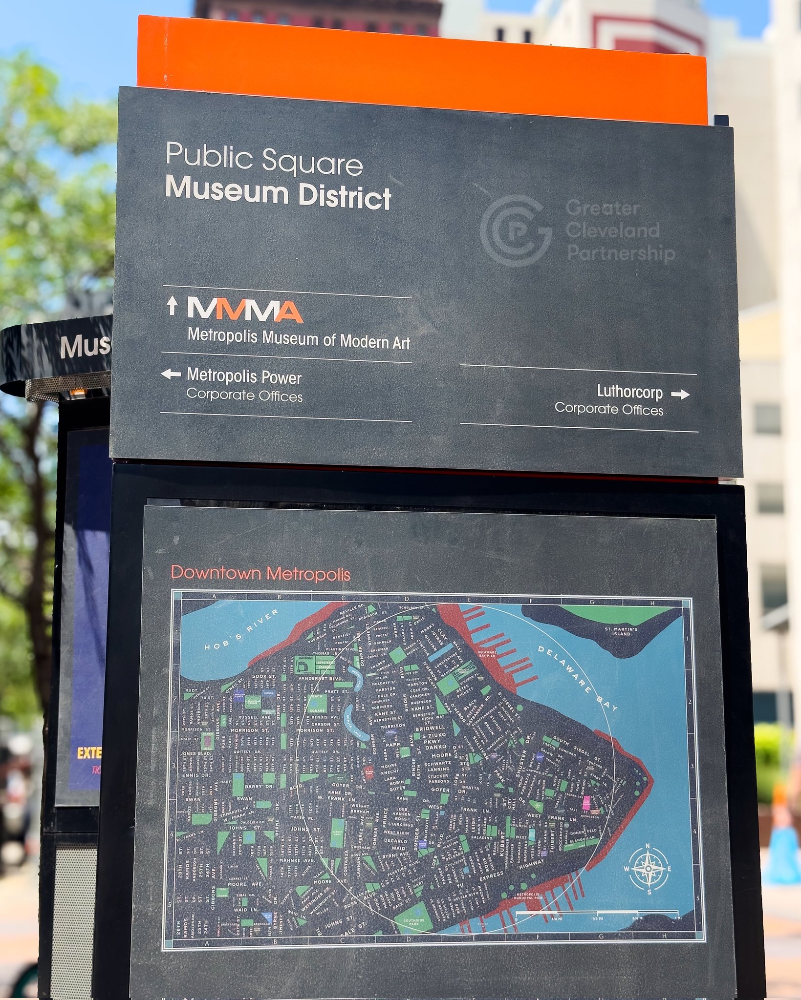 A sign for Public Square Museum District lists locations like the Museum of Modern Art and corporate offices, above a detailed map labeled Downtown Metropolis.
