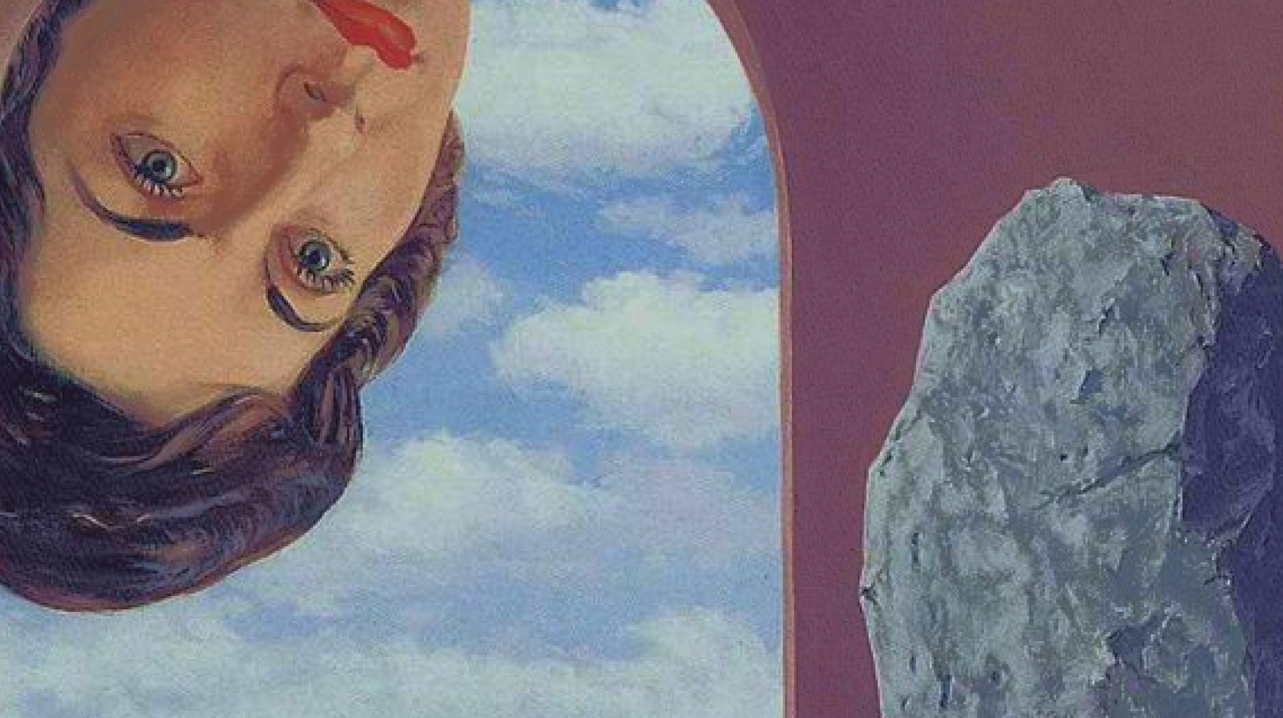 A painted woman's face is seen upside down on the left, looking at a large gray rock on the right, with a blue sky and clouds in the background.