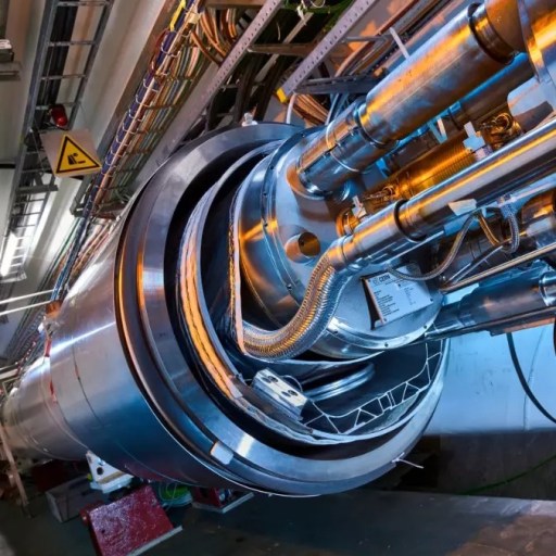 A person inspects a large, cylindrical section of a Higgs factory tunnel lined with metal pipes, cables, and equipment—a crucial site for particle physics research.