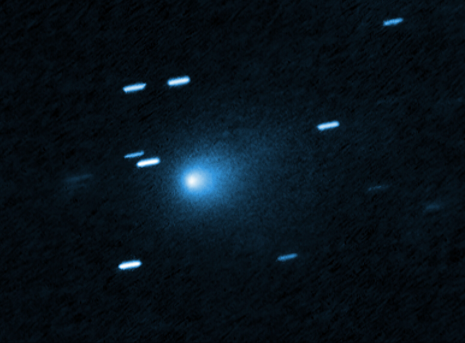 A bright SPHEREx comet 3I/ATLAS with a glowing core and faint tail is seen against a dark background, surrounded by several streaks of light representing stars.