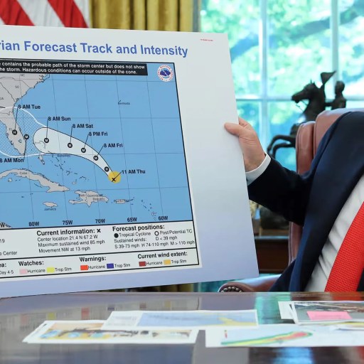A person in a suit holds up a NOAA map showing the forecast track and intensity of Hurricane Dorian, reminding us that, unlike Einstein, we can't change the facts—only prepare for them—in an office setting.
