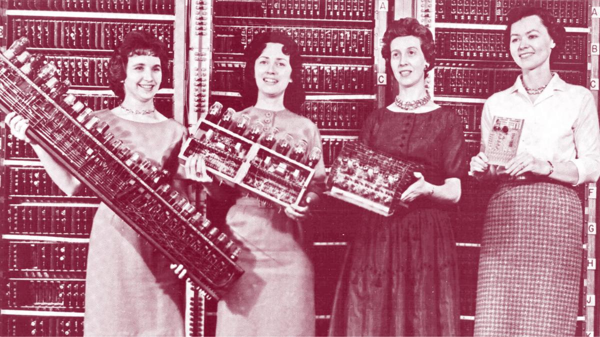 Four women stand in front of a vintage computer, each holding different components of its hardware, with the computer's panel visible in the background—an image reminiscent of historical innovation studied by Angus Fletcher.