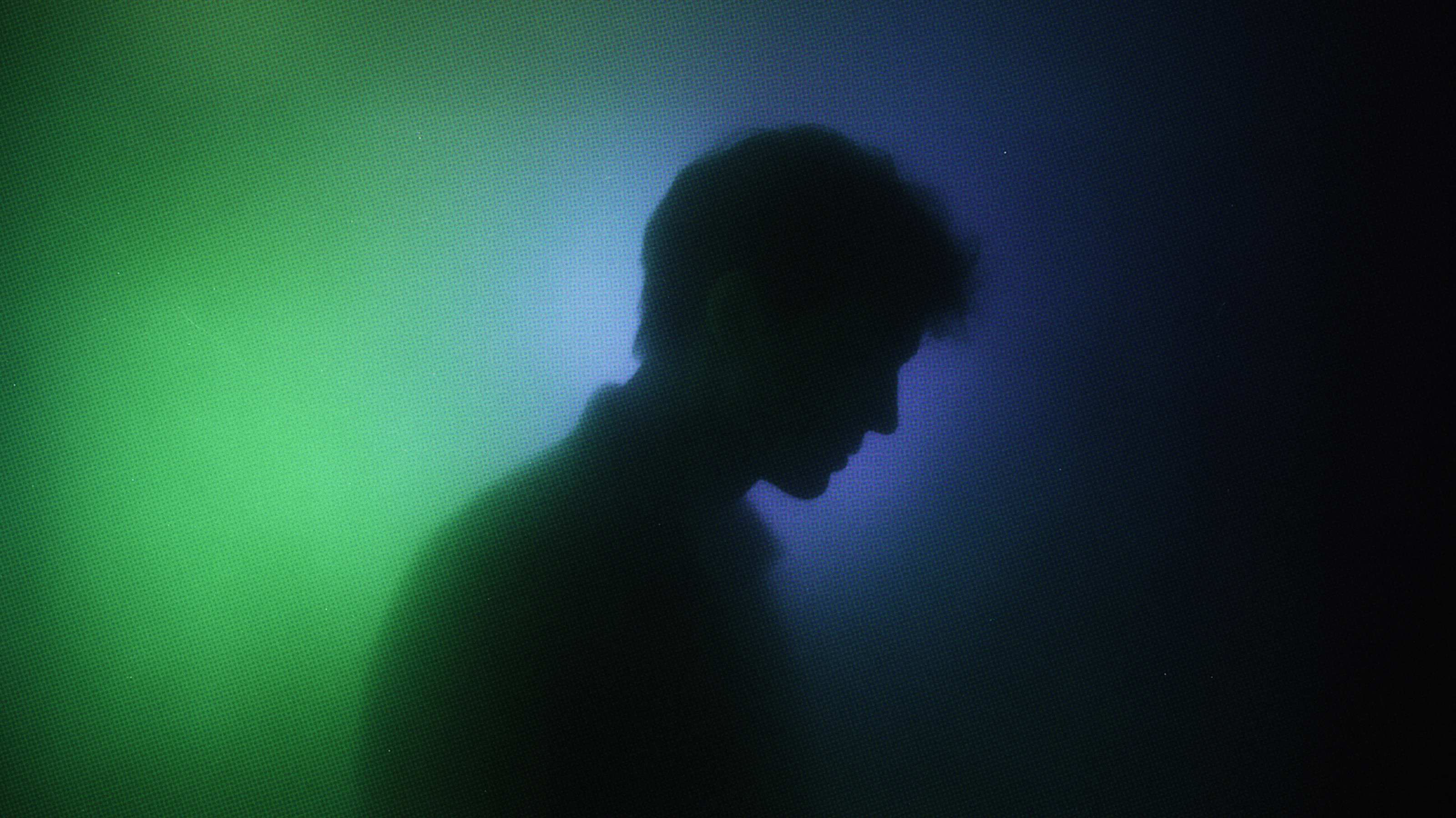 Silhouette of a person in profile against a gradient background of green and blue light.