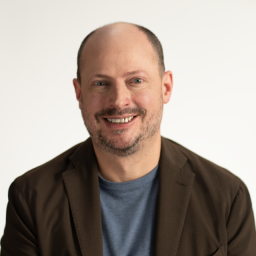 A man in a blazer sitting in front of a white backdrop