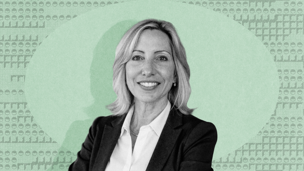 Susan Schneider, in a business suit, smiles at the camera, with a green patterned background behind her.