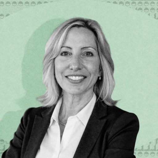 Susan Schneider, in a business suit, smiles at the camera, with a green patterned background behind her.