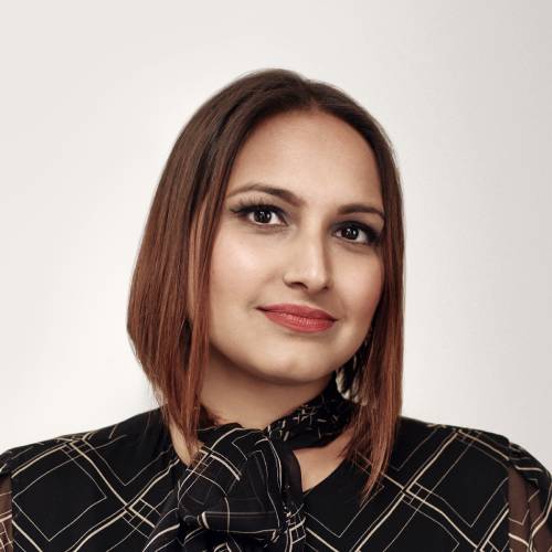 A woman with straight, shoulder-length brown hair, wearing a black top with a geometric pattern and a bow at the collar, poses against a light background.
