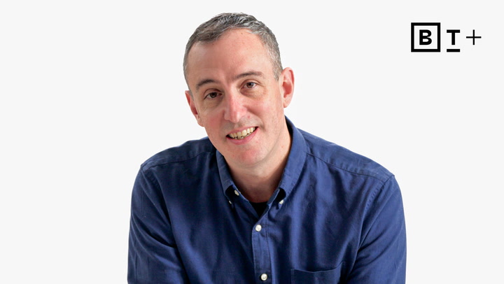 A man in a blue button-up shirt smiles at the camera against a plain white background, with a "B T +" logo in the top right corner.