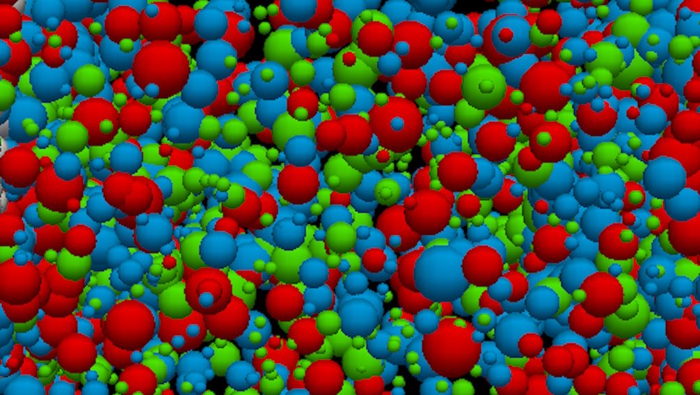 A dense cluster of differently sized red, blue, and green spheres overlaps against a black background, evoking the biggest mysteries surrounding the origin of the universe.