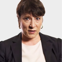A woman with short brown hair and gold hoop earrings, wearing a black blazer and white top, has a surprised or concerned facial expression against a plain background.