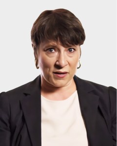A woman with short brown hair and gold hoop earrings, wearing a black blazer and white top, has a surprised or concerned facial expression against a plain background.