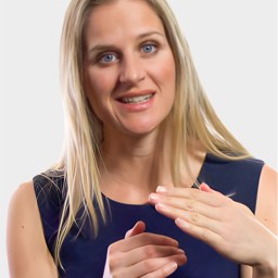A woman with long blonde hair and a navy sleeveless top gestures with her hands while smiling at the camera against a plain light background.