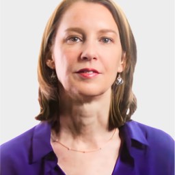 A woman with shoulder-length brown hair, wearing a purple blouse, drop earrings, and a delicate necklace, poses against a plain light background.