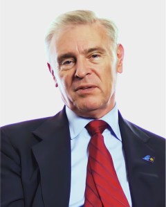 A middle-aged man with short, gray hair in a dark suit, light blue shirt, and red striped tie, facing the camera against a plain white background.