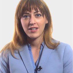 A woman with light brown hair wearing a light blue blazer and a blue shirt, speaking and facing the camera against a plain white background.