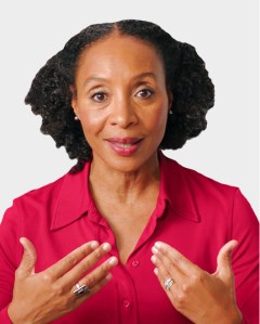 A woman with curly hair wearing a red collared shirt gestures with both hands while looking forward.